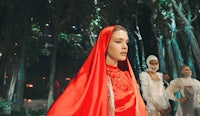 a woman in a red cloak is standing in a forest