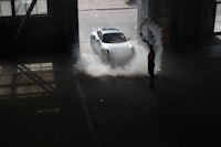 a man standing in front of a car with smoke coming out of it