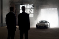 two men standing in front of a porsche car in a warehouse